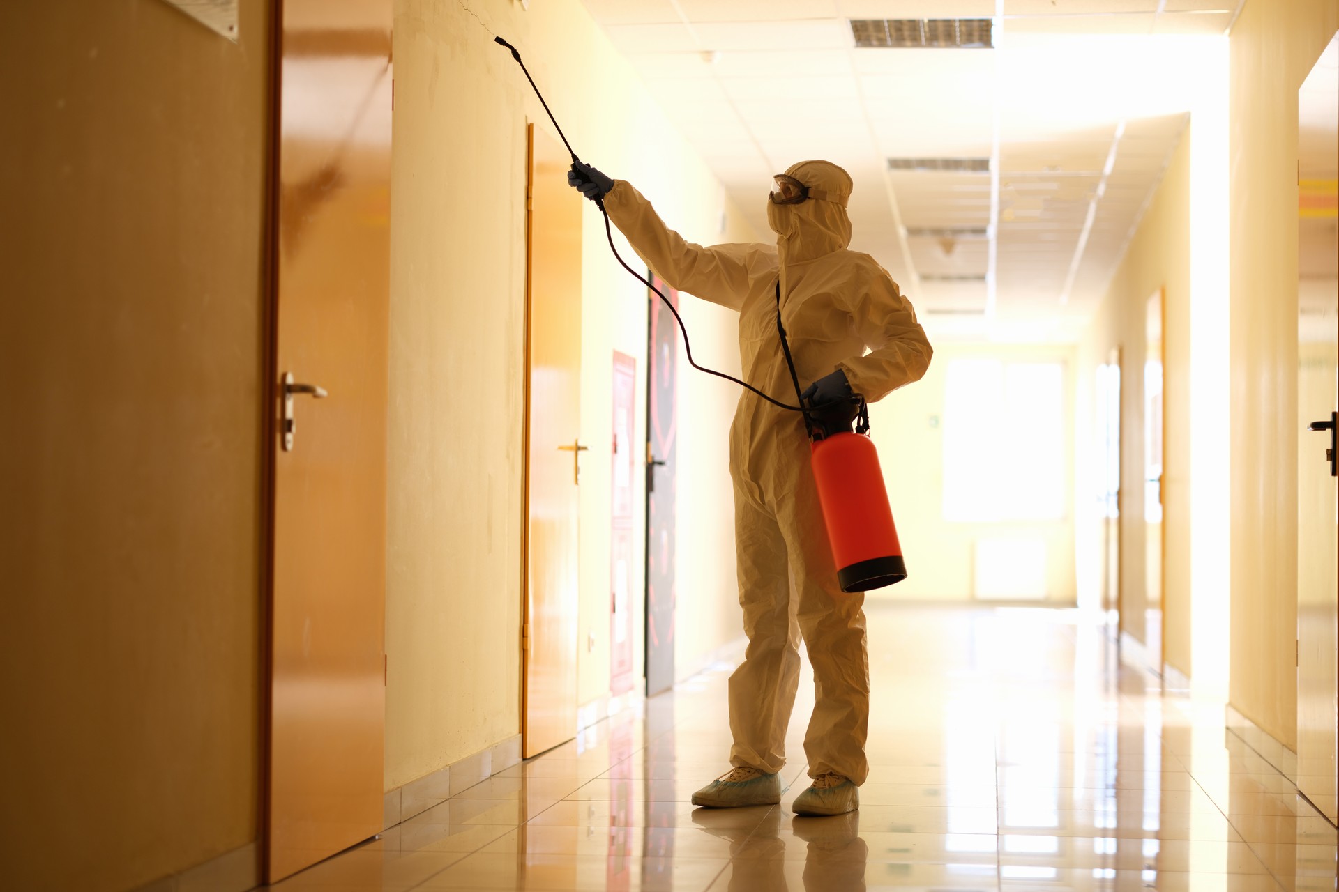 Person wearing white chemical protection suit holding spray bottle with disinfectant chemicals